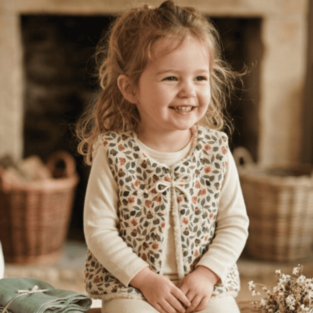 Petite fille portant un gilet de berger enfant fleuri en gaze de coton et moumoute écru.