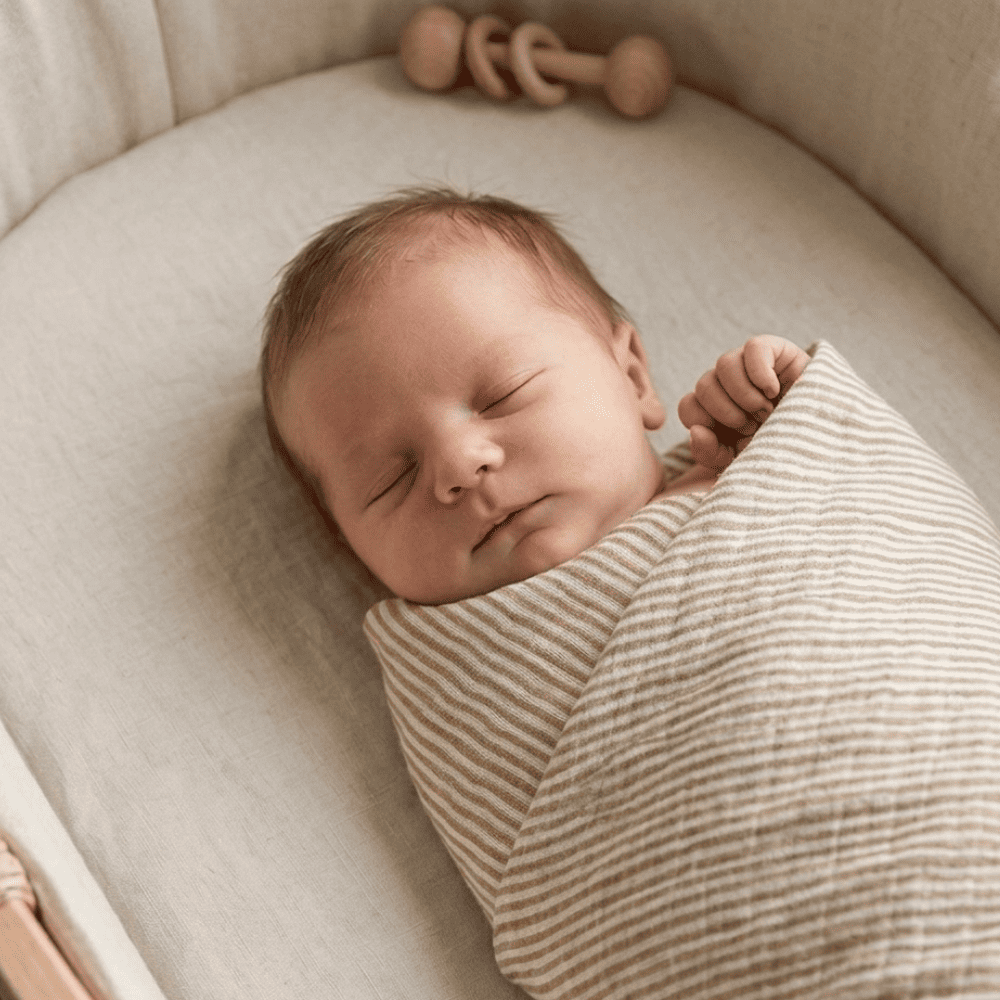 Nouveau-né paisible endormi, emmailloté dans un lange rayures camel et écru
