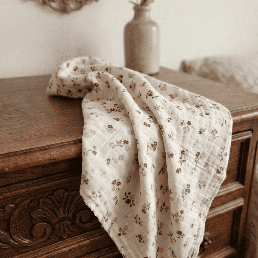 ange bébé en gaze de coton bio motif petites fleurs roses posé sur une commode en bois vintage avec vase d'eucalyptus.