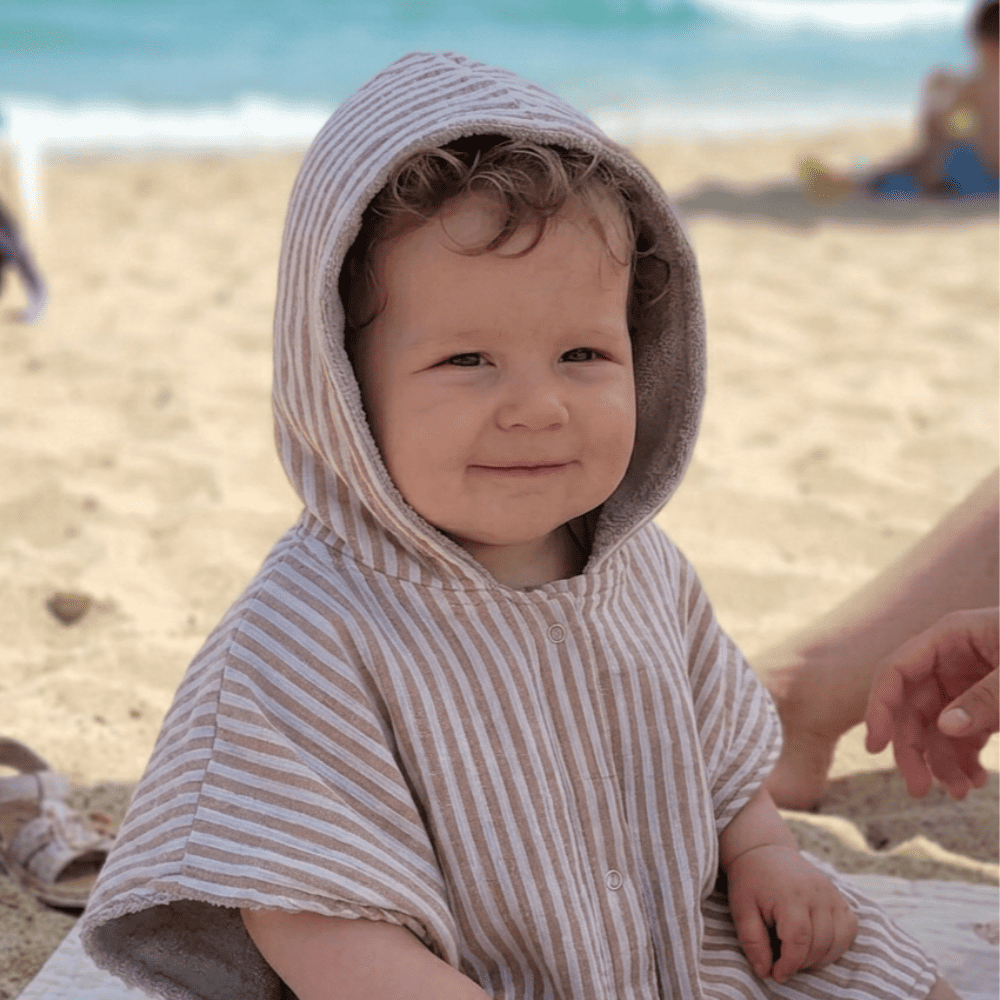 bébé portant sur la plage un poncho à capuche rayé camel et écru