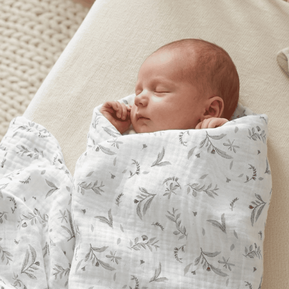 Nouveau-né endormi emmailloté dans un lange blanc en gaze de coton avec imprimé floral doux.