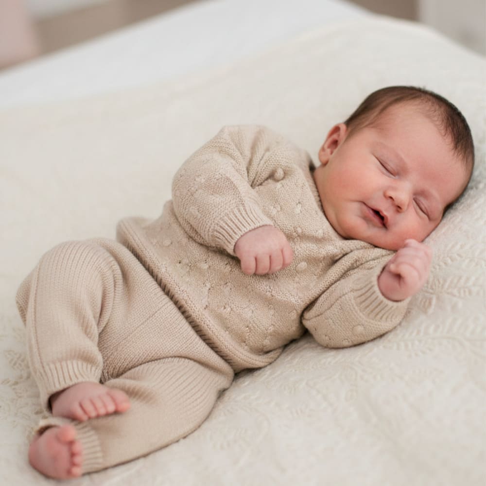 Bébé habillé avec l'ensemble beige les petits basique, qui dort sur un lit