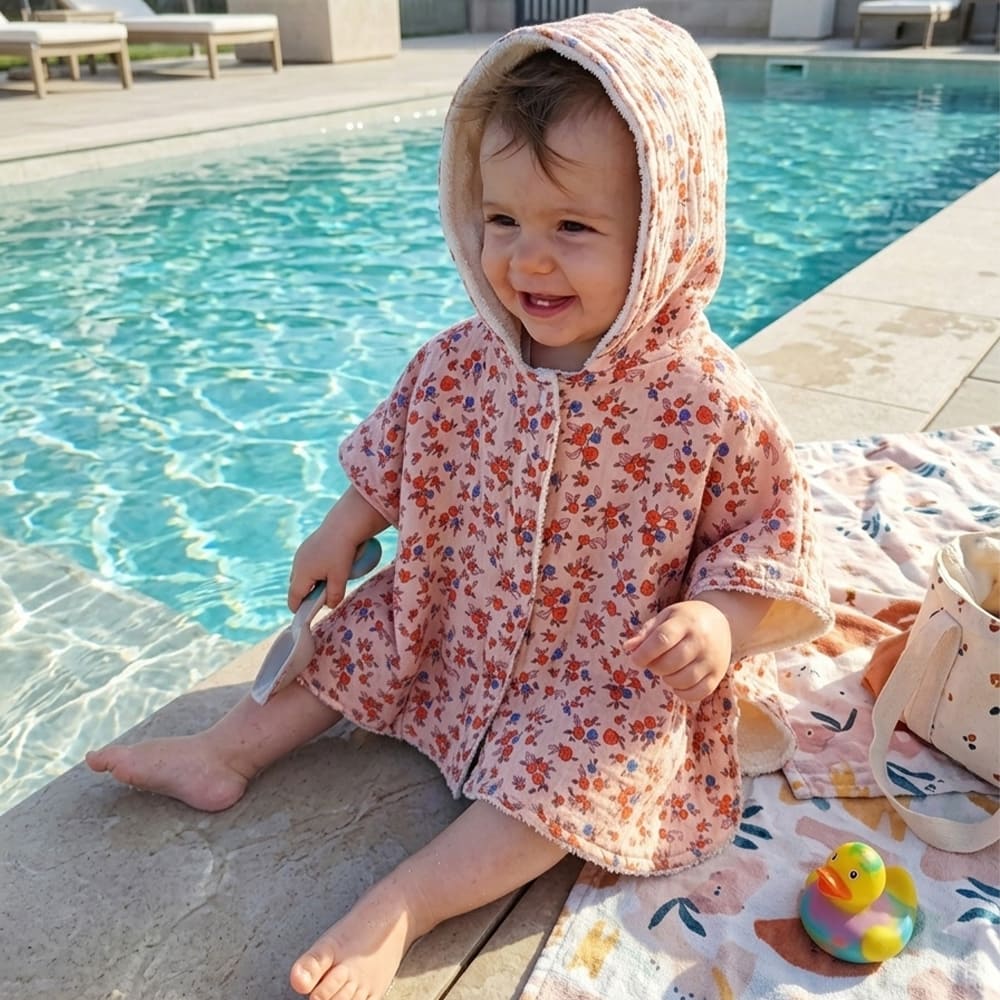 Bébé sur le bord de la piscine dans le poncho de bain fleurs de printemps, à motifs de fleurs rouges et bleues foncées