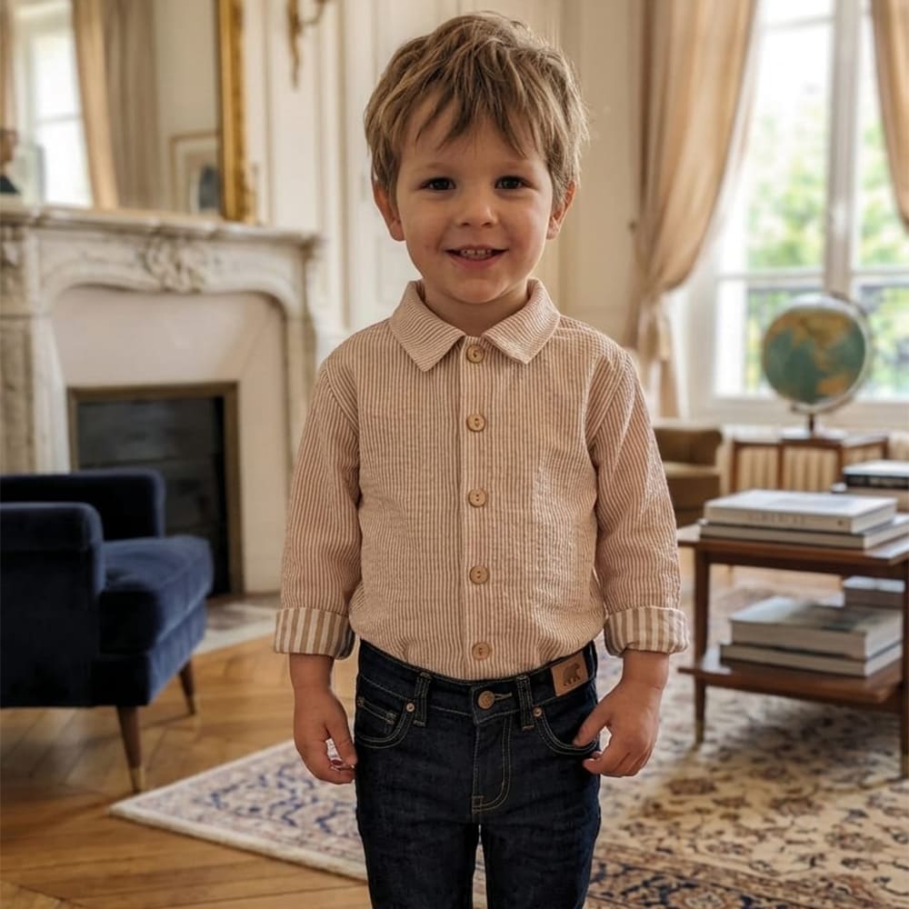 Un petit garçon qui porte la chemise méridien, à petites rayures d'un côté et grosses rayures au niveau des manches repliées