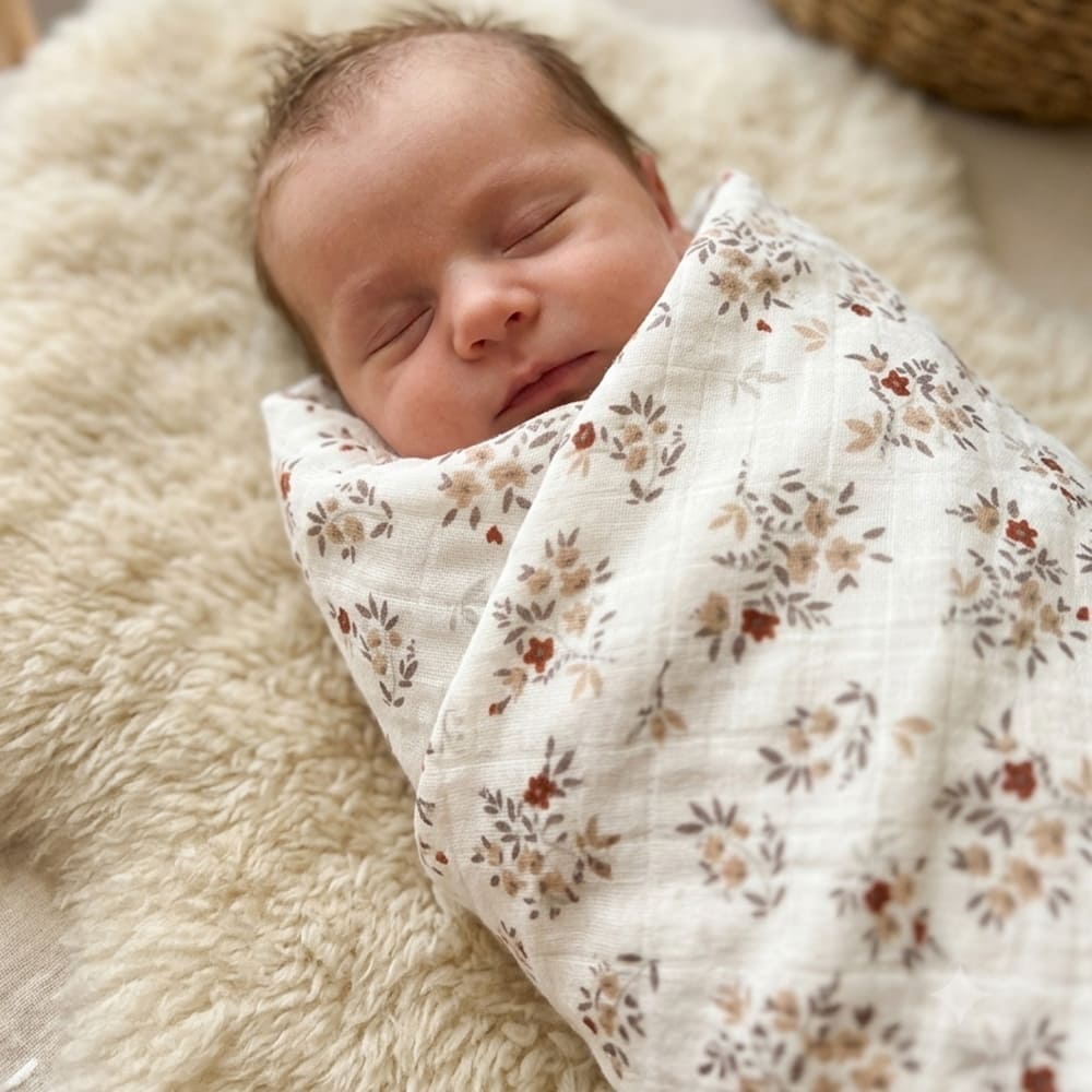Bébé emmailloté dans le maxi lange Agathe, aux motifs fleuris gris et rouges