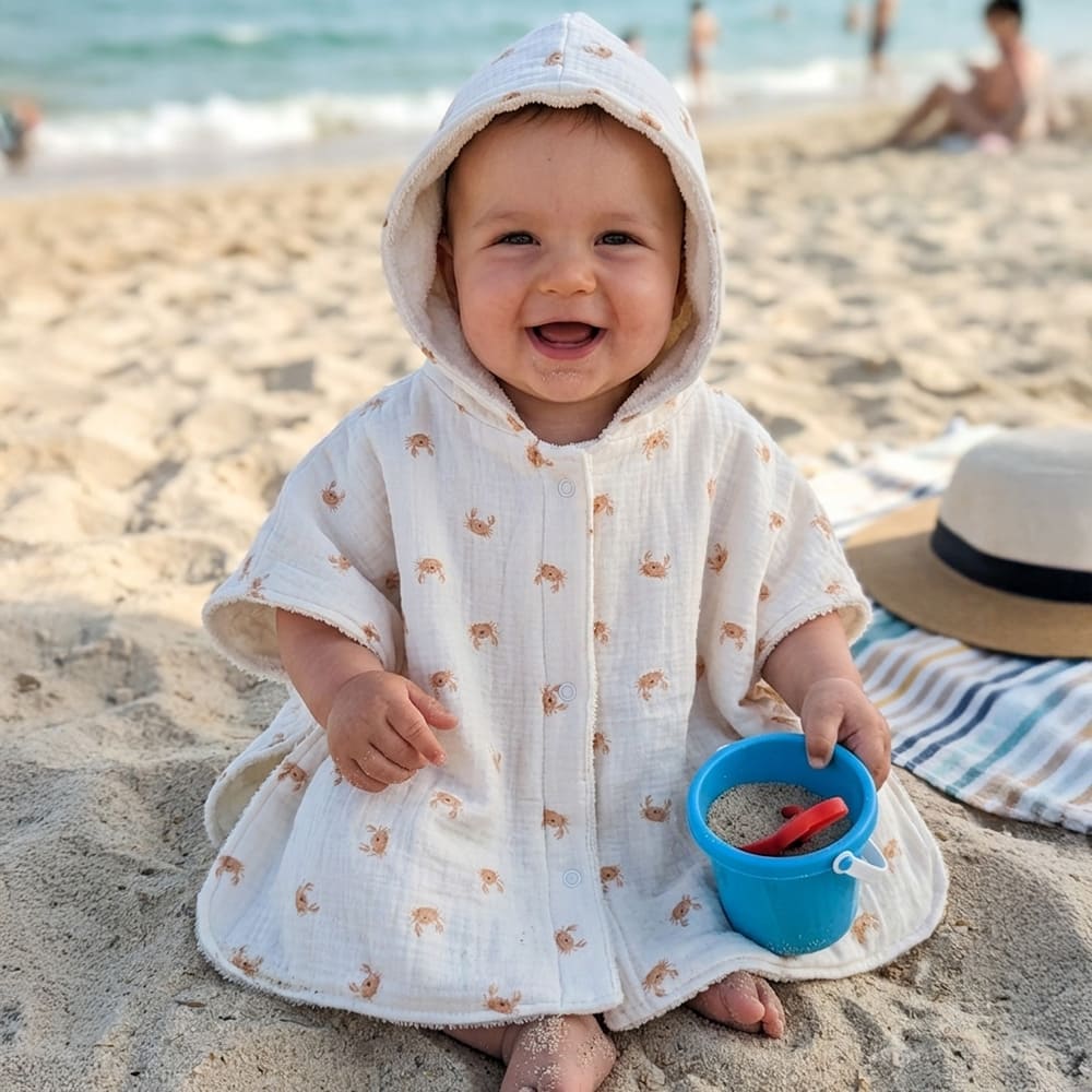 Bébé qui porte le poncho de bain Les Petits Crabes, blanc à motifs de crabes oranges
