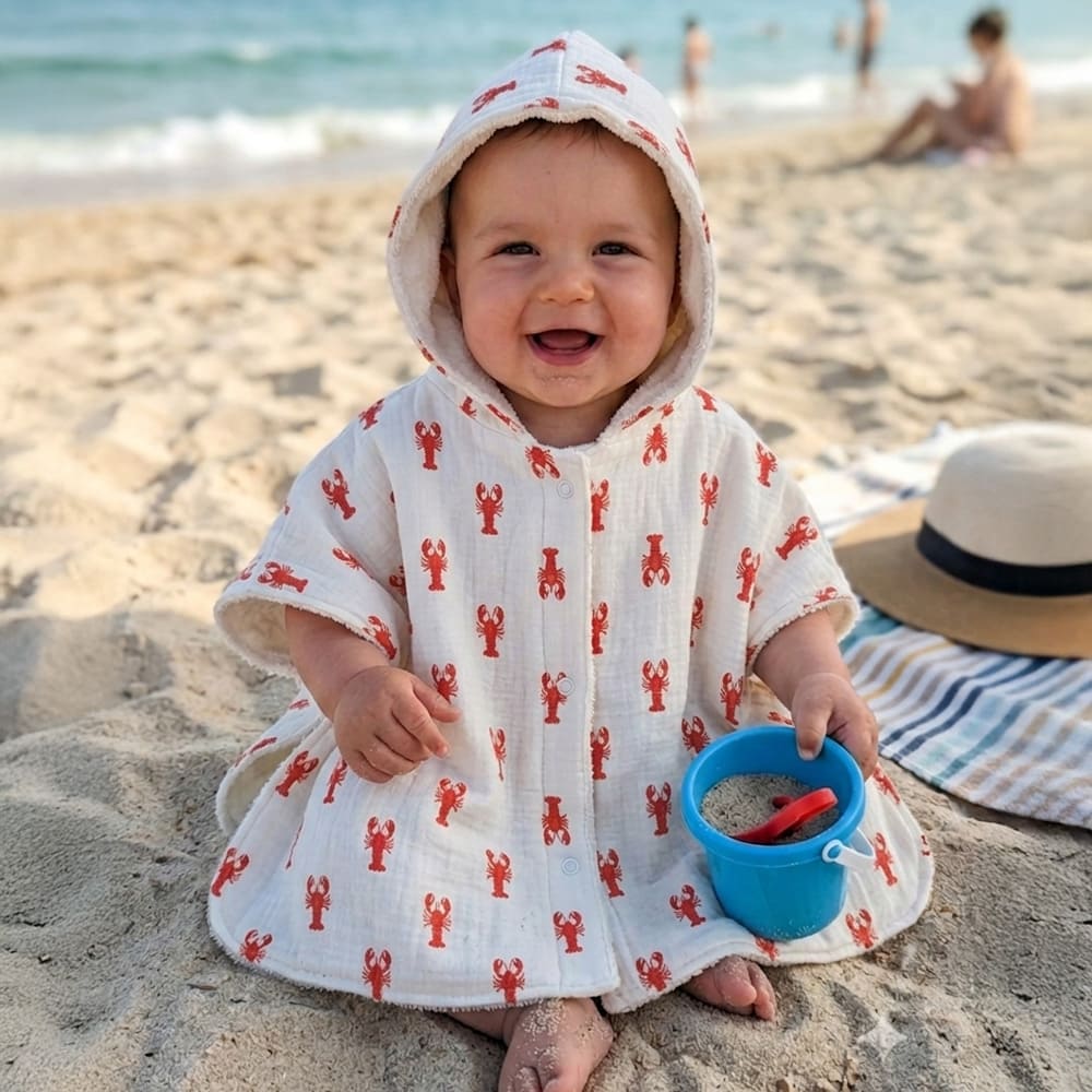Bébé qui porte le poncho Les Petits Homards, blancs aux motifs rouges de homards
