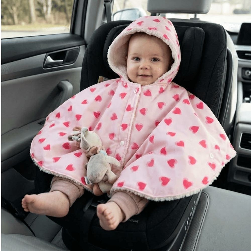 Petite fille qui porte le poncho de voiture rose avec des motifs de cœurs